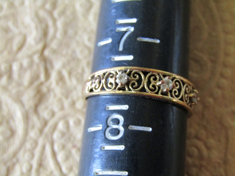 May include: A gold band ring with a delicate filigree design and small clear stones. The ring is sized for a size 8 finger.