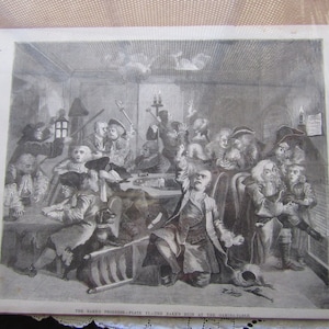 May include: A black and white engraving depicting a group of people gathered around a table, likely playing cards. The scene is set in a dimly lit room with a chandelier hanging from the ceiling. The engraving is titled "The Rake's Progress - Plate VI - The Rake's Run at the Gaming Table."