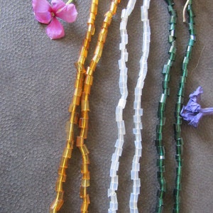 May include: Three strands of square-shaped beads, one amber, one white, and one green. The beads are strung on a thin cord and are arranged in a row.