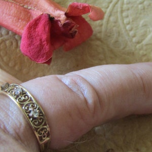 May include: A gold ring with a delicate filigree design and small clear stones. The ring is worn on a person's thumb.