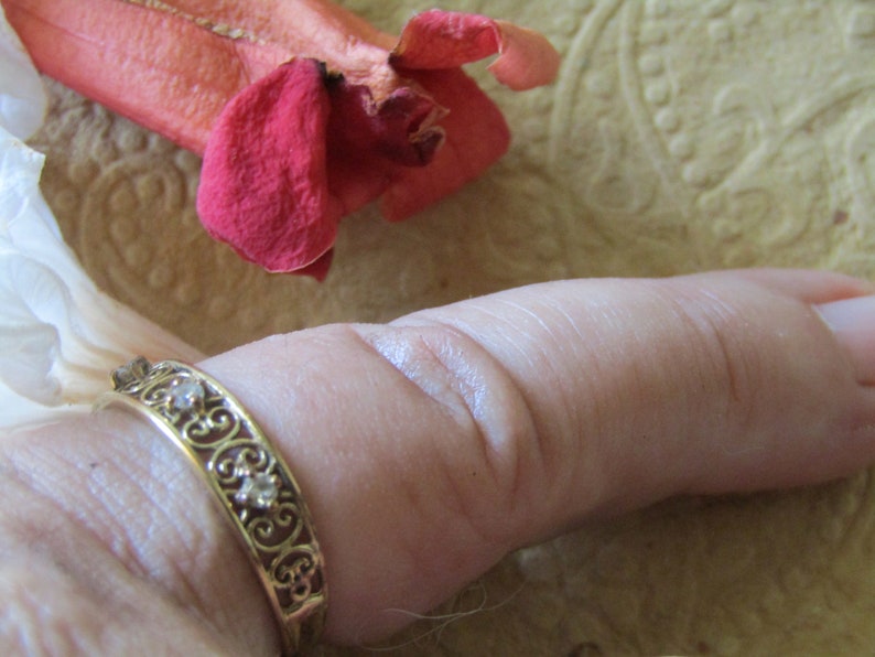 May include: A gold ring with a delicate filigree design and small clear stones. The ring is worn on a person's thumb.