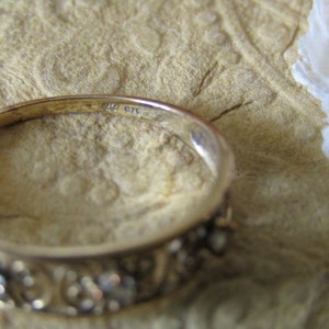 May include: A gold band ring with a decorative design and small stones. The inside of the band is marked with the number "10 G14".