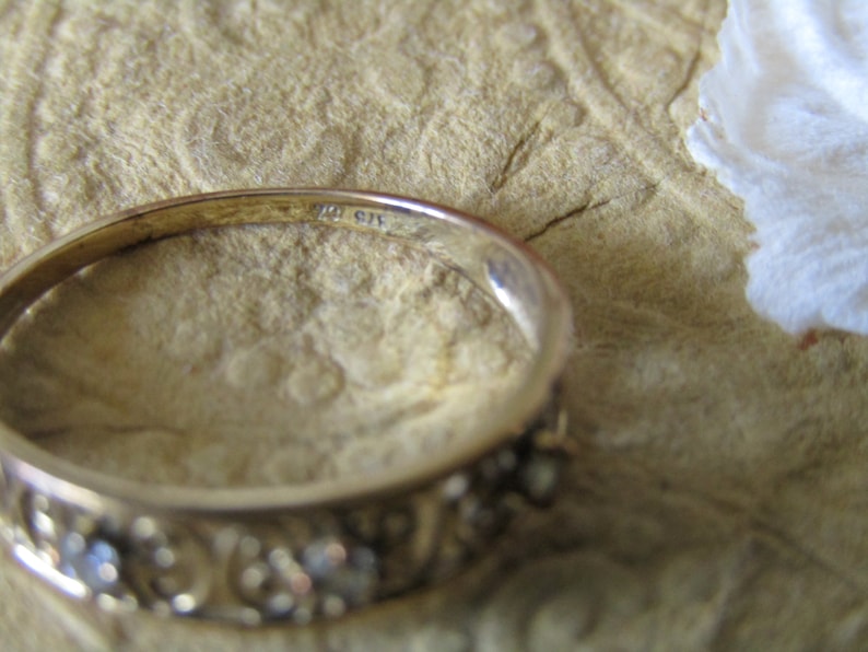 May include: A gold band ring with a decorative design and small stones. The inside of the band is marked with the number "10 G14".