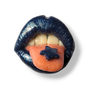 May include: Close-up of a pair of blue glitter lips with a pink tongue sticking out. A blue glitter star is on top of the tongue.