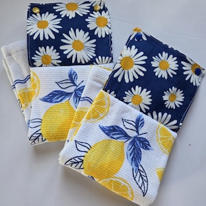 May include: A selection of kitchen towels and pot holders. The towels display a white background with yellow lemons and blue leaves. The pot holders have a navy blue background with white daisies. The text "Les Trésors de Sylvie" is at the bottom.