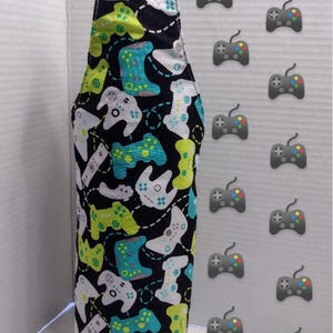 May include: A black fabric bottle holder with a white strap. The fabric has a pattern of green, white, and blue video game controllers. The text "Gamers" is at the top of the image. The text "Les Tresors de Sylvie" is at the bottom of the image.
