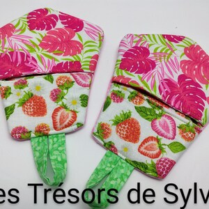 May include: Two fabric pot holders with a tropical floral and strawberry design. The top section features pink flowers on a white background, while the bottom has strawberries and daisies. Green handles.