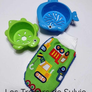 May include: A set of three bath toys for babies and toddlers. The set includes a blue whale-shaped bath strainer, a green turtle-shaped bath strainer, and a green washcloth with a white trim and a construction vehicle pattern. The washcloth has a textured surface for gentle scrubbing.