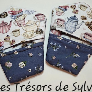 May include: Two fabric tea cosy covers. The top section has a pattern of teacups, teapots, and pastries. The bottom is a dark blue floral print. The text "Les Trésors de Sylvie" is at the bottom.