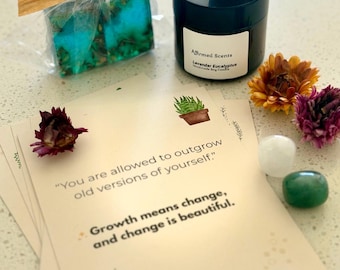 May include: A gift set featuring a teal and green soap bar, a black candle with the text "Affirmed Scents Lavender Eucalyptus", and affirmation cards. The cards have the text "You are allowed to outgrow old versions of yourself." and "Growth means change, and change is beautiful."