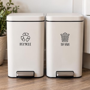 Könnte beinhalten: Zwei rechteckige weiße Treteimer mit schwarzem Rand. Der linke Eimer zeigt ein schwarzes Recycling-Symbol und den Text RECYCLE. Der rechte Eimer zeigt ein schwarzes Mülleimer-Symbol und den Text TRASH. Beide haben ein silbernes Metallpedal.