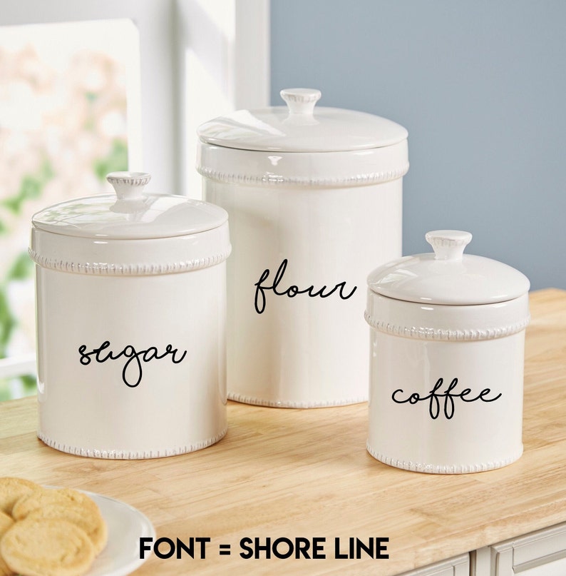 May include: Set of three white ceramic canisters with black script labels reading "sugar", "flour", and "coffee".