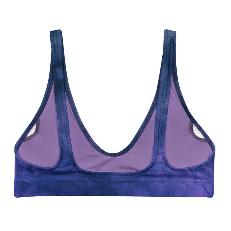 A back view of the bikini top laid flat. There is an area to remove the padding. The color is a deep purple with hits of blue in a tie dye pattern.