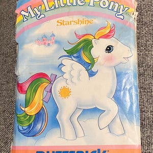 May include: A Butterick sewing pattern envelope for a My Little Pony Starshine character. The front features a white winged pony with a rainbow mane and tail, a yellow star symbol, and a pink castle in the background. Text includes 3212.