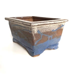 Könnte beinhalten: Ein rechteckiger Bonsai-Topf aus Keramik mit einer blauen, braunen und weißen Glasur. Der Topf hat vier Füße und einen leicht ausgestellten Rand.