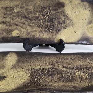 Peut inclure: Deux assiettes rectangulaires en céramique présentant une surface texturée et tachetée avec un mélange de tons brun foncé et jaune sourd. Les assiettes ont des bords légèrement relevés et une finition rustique, l'une étant sur un support noir.