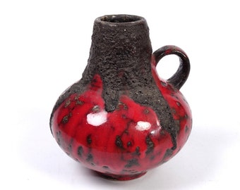 May include: A red and black ceramic vase with a textured surface and a small handle. The vase has a rounded body and a narrow neck.