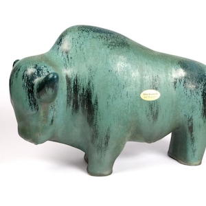 Peut inclure: Une sculpture de bison en céramique de couleur vert d'eau et vert foncé. La figurine a une surface texturée et une étiquette sur le côté. Le bison est debout sur quatre pattes et a de petites oreilles.