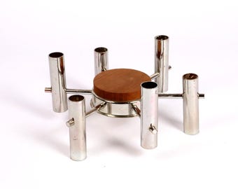 May include: A silver-toned metal candle holder with six cylindrical openings. The holder features a circular wooden base and horizontal supports. The design is modern and minimalist, suitable for home decor.