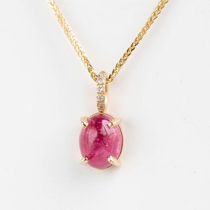 Vivid pink tourmaline necklace prong set in 14K solid gold. It is attached to a ring with 5 diamonds and a braided solid gold chain passes through it.