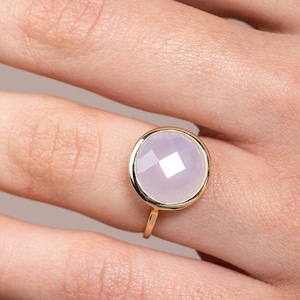 Puede incluir: Un anillo de oro con una gran piedra preciosa redonda, facetada, de color púrpura claro.