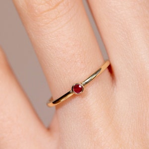 Könnte beinhalten: Ein schlichter Goldring mit einem kleinen, runden, roten Edelstein.