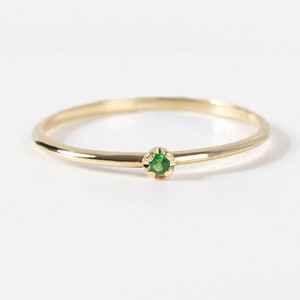 Puede incluir: Un delicado anillo de banda de oro con una pequeña piedra preciosa verde redonda engastada en el centro.