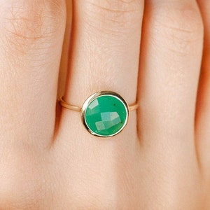 Round faceted chrysoprase gemstone ring in 14K yellow gold on the middle finger of a woman.