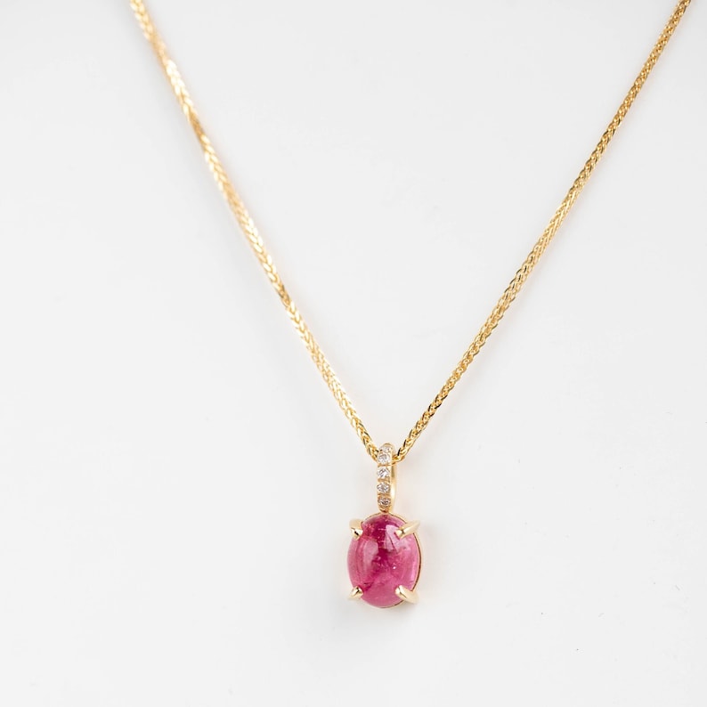 Vivid pink tourmaline necklace prong set in 14K solid gold. It is attached to a ring with 5 diamonds and a braided solid gold chain passes through it.