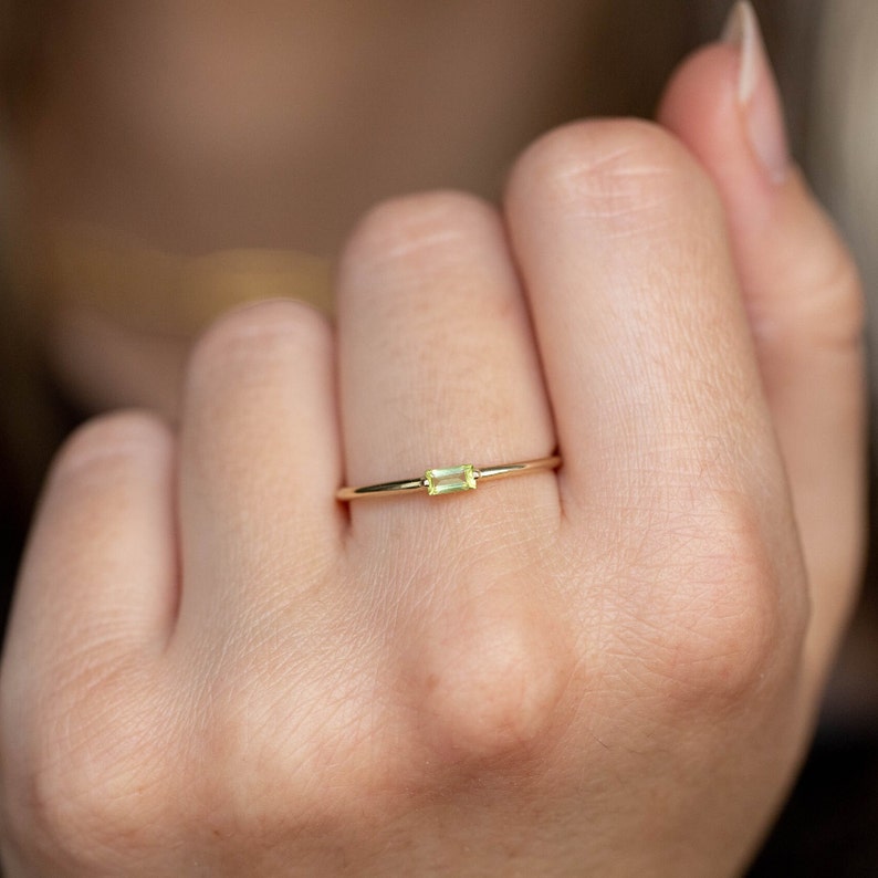Minimalist green peridot ring in 14K solid yellow gold on the middle finger of the model.