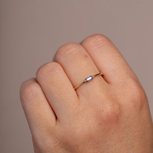 Thin solid gold ring with a natural baguette blue sapphire gemstone on the middle finger of a woman's hand.