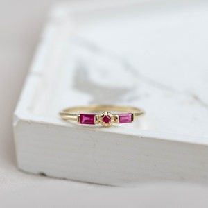 Genuine ruby ring, baguette and round, in 14K yellow gold on a white marble plate.