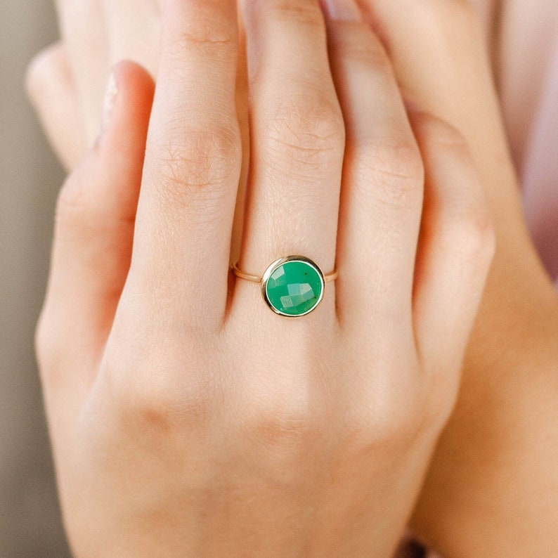 Round faceted chrysoprase gemstone ring in 14K yellow gold on the middle finger of a woman.