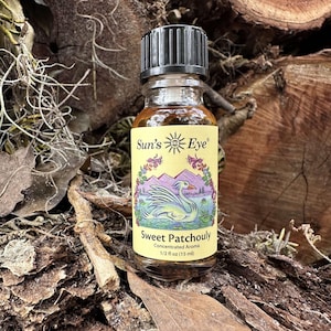 May include: A small glass bottle of Sweet Patchouly concentrated aroma. The label features a swan on a lake with mountains and the text "Sun's Eye". The bottle is 1/2 fl oz (15 ml).
