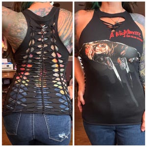 May include: A black sleeveless top featuring a graphic print of a character with bladed fingers and the text A Nightmare on Elm Street. The front neckline has a lace-up detail, while the back is constructed with a series of horizontal cutouts.