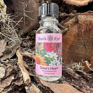 May include: A clear glass bottle with a black ribbed cap containing Sun's Eye Dove's Heart concentrated aroma. The pink label features a colorful floral illustration and the text: Sun's Eye, Dove's Heart, Concentrated Aroma, 1/2 fl oz (15 ml).