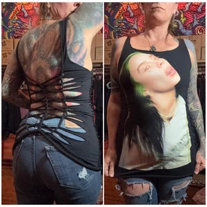 May include: Black tank top with a cut-out back design and a Billie Eilish graphic on the front. The tank top is paired with blue denim jeans with distressed details.