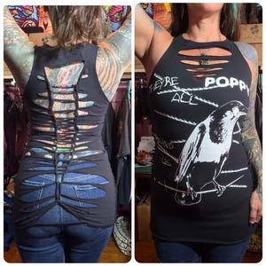 May include: A black sleeveless tank top featuring a white graphic of a bird perched on a wire with the text "THEY'RE ALL POPPY AROUND US". The front neckline has horizontal cutouts, and the back features a vertical woven lattice design.
