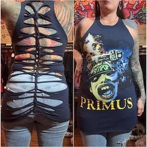 May include: Navy blue tank top with a distressed back design. The front features a graphic print with the word "PRIMUS" in yellow. The graphic includes the word "ANTIPOP" and a green and yellow face.