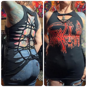 May include: Black tank top with a cut-out back design, laced with black fabric. The front features a red graphic of the word "Death". The top is paired with blue jeans. A unique, edgy style.