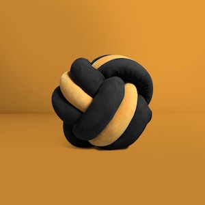 May include: A black and yellow knotted pillow. The pillow is made of soft fabric and has a unique, knotted design.