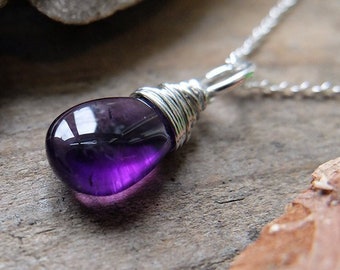 May include: A silver chain necklace with a purple amethyst gemstone pendant wrapped in silver wire. The pendant is on a wooden surface.