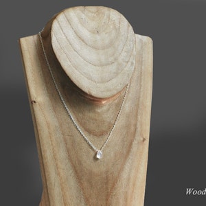 May include: A silver chain necklace with a teardrop-shaped pendant on a wooden display stand. The pendant is a milky white color.