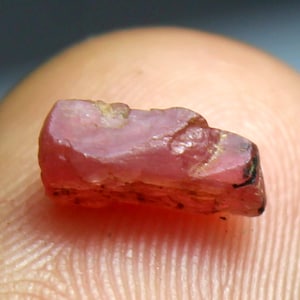May include: A pink ruby gemstone with a rough, natural finish. The ruby is a deep pink color and has a slightly translucent appearance.