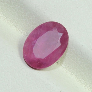 Pode incluir: Gema de rubi facetada em forma oval. A gema é de cor rosa profundo com facetas rosa mais claras. A pedra está sobre um fundo branco.