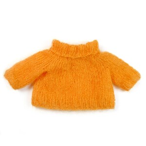 Puede incluir: Un jersey de punto naranja brillante para una mu&ntilde;eca o un peque&ntilde;o animal de peluche. El jersey tiene cuello alto y mangas largas.