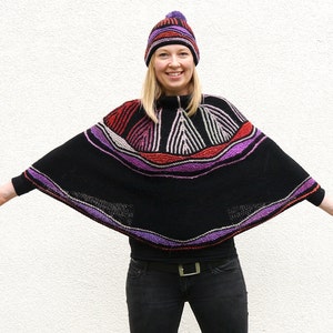Könnte beinhalten: Eine Frau trägt einen schwarzen Strickponcho mit bunten Streifen und eine lila-rote Strickmütze. Der Poncho hat eine weite, fließende Form und wird über einem schwarzen Shirt und Jeans getragen.