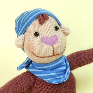 May include: A knitted toy monkey wearing a blue and white striped hat and scarf. The monkey has brown yarn hair, brown eyes, and a pink nose.