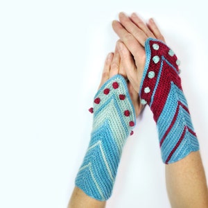May include: A pair of blue and red fingerless gloves with a chevron pattern and red pom-poms.