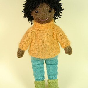May include: A knitted doll with brown skin, black curly hair, a yellow sweater, blue pants, and green boots.